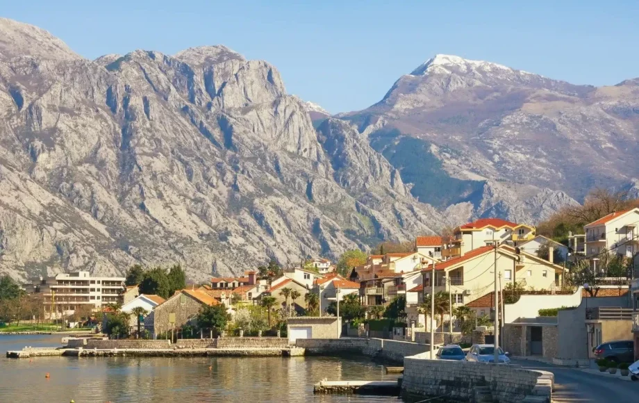 Scenic view of Bay of Kotor, Montenegro, with traditional terracotta-roofed houses and towering mountain backdrop.