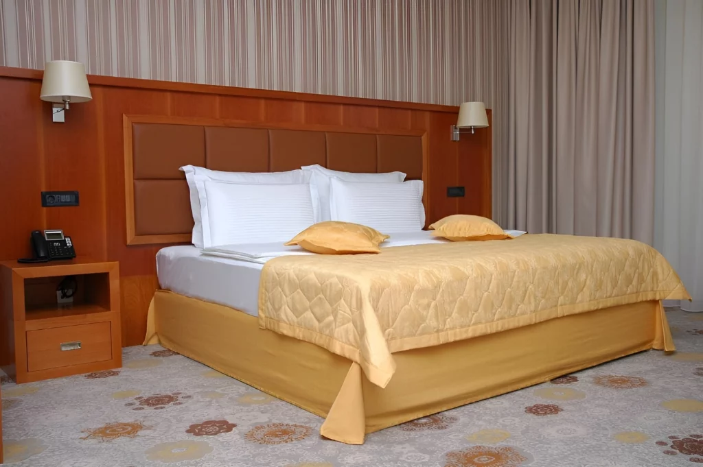 Double room bedroom in Kings Park Hotel in Montenegro with a king-size bed, golden bedspread, bedside lighting, and elegant wooden decor.