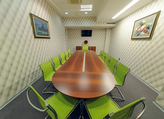 Modern conference room at Kings Park Hotel featuring a sleek wooden table, vibrant green chairs, equipped with a flat-screen TV for presentations.