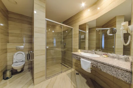 Modern hotel bathroom in Kings Park Hotel featuring a walk-in shower, marble vanity, and full-length mirror, reflecting a clean and luxurious design.