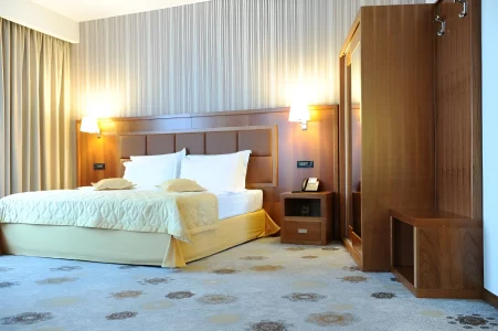 Luxury Double room at Kings Park Hotel with a large bed adorned with yellow accents, contemporary wooden furnishings, and soft lighting, offering a serene vacation in Montenegro.