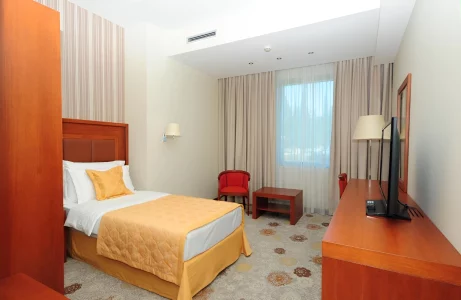 Montenegro Hotel room with a single bed featuring yellow bedding, a simple work desk and chair, and a window with sheer curtains, providing a comfortable and bright space for guests.