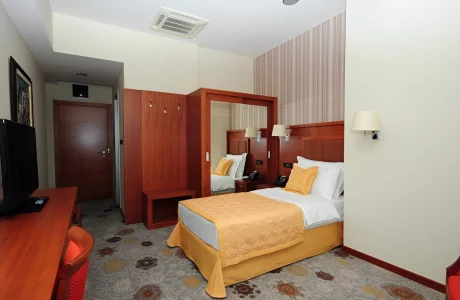 Single bedroom at Kings Park Hotel Podgorica with a comfortable bed, warm yellow accents, and wood-paneled walls, offering a homey atmosphere for guests.